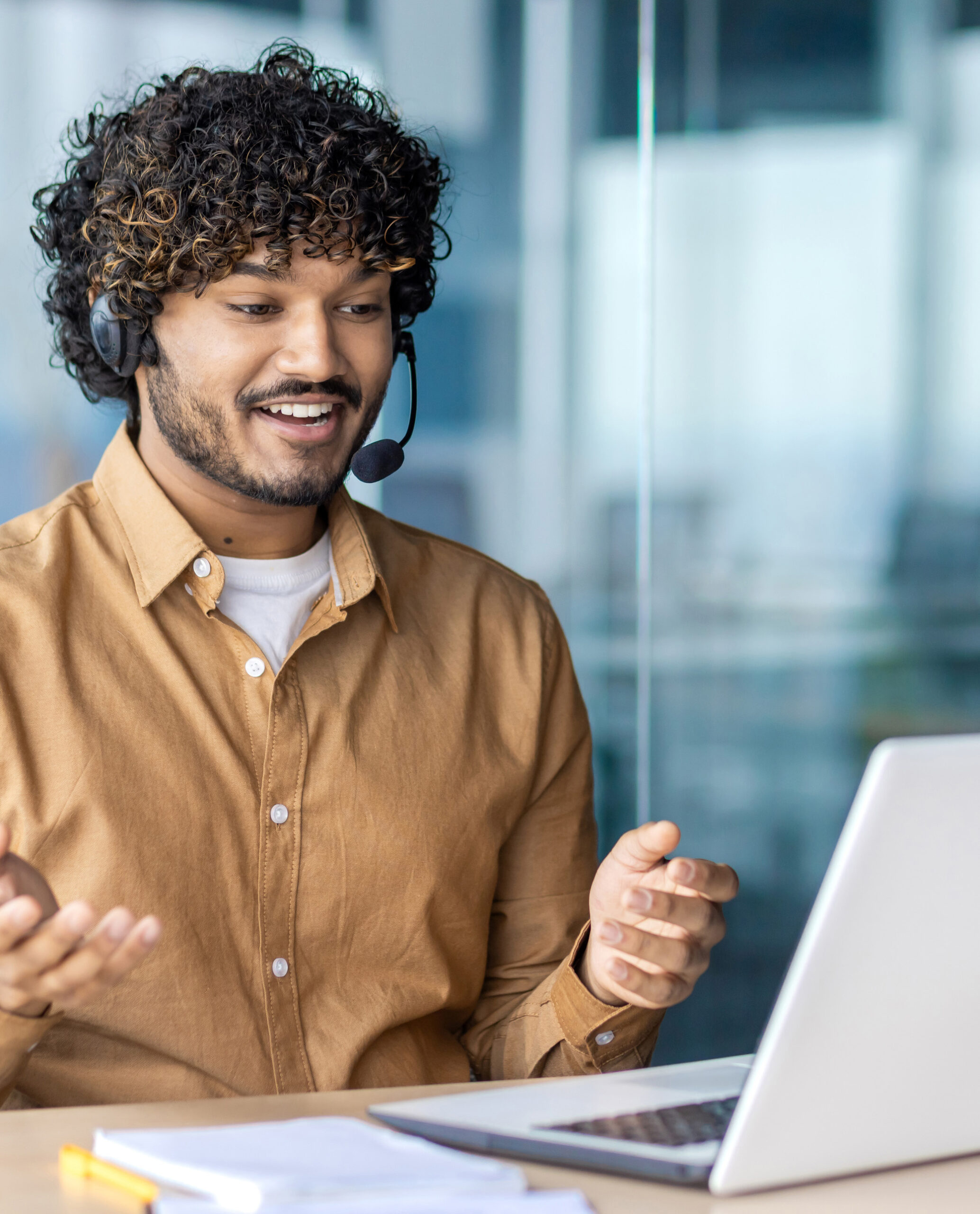Worker with headset phone for video call talking to buyers customers consulting remotely, businessman working inside office with laptop sitting at desk